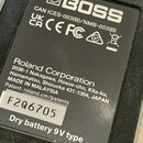 Fotografie detailu spodní strany efektového pedálu s černým štítkem. Na štítku je bílé logo BOSS a nápisy CAN ICES-003(B)/NMB-003(B), UK CA, CE a FC…
