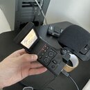 Černý přenosný digitální záznamník s vyklopeným displejem a připojeným mikrofonem s černou větrovicí. Na horním panelu jsou vidět červené kontrolky u…