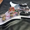 Bílá pickguard s namontovanou elektronikou a třemi snímači. Snímače jsou v provedení dvou černých humbuckerů a jednoho středového snímače s bílým pla…