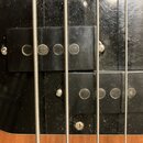 Detailní pohled na dvě černé snímače basové kytary s čtyři viditelnými póly každý. Snímače jsou umístěny na černém plastovém pickguardu, který vykazu…