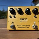 Zlatý efekt pedál s nápisy MXR a BASS INNOVATIONS. Na horní straně jsou čtyři černé oválné knoflíky s popisky GAIN, FUZZ, OCTAVE a DRY. Ve spodní čás…