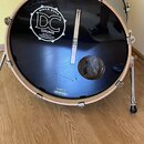 Černý basový buben s kovovým obručem a stěnou v stříbrné barvě. Na přední koži je bílé logo s nápisy SINCE 2004, DC DRUMS a QUALITY HANDCRAFTED WOODS…