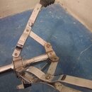 Detailní pohled na chromovaný mechanismus pedálu bicích. Povrch vykazuje známky opotřebení, drobné škrábance a oxidaci v místech spojů. Na horní část…