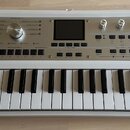 Bílá klávesová syntezátor s nápisem KORG microKORG synthesizer vocoder. Přístroj má v horní části ovládací panel s několika otočnými knoflíky, tlačít…