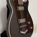 Tmavně hnědá polodupatá elektrická kytara s černým pickguardem a bílým lemováním. Na pickguardu je viditelné logo GRETSCH. Nástroj má dva snímače s k…