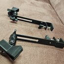 Dvě černé kovové ramena pro uchycení mikrofonů nebo příslušenství. Každé rameno má na jednom konci svorku a na druhém kloubový mechanismus s držákem.…
