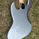 Zadní strana elektrické kytary v šedé barvě s kovovými šrouby u krku. Na černém plastovém krytu spojení krku s tělem je bílé logo Squier Fender. Povr…