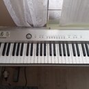 Stříbrošedý elektronický klavír s bílými a černými klávesami. Na levé straně je vidět logo CASIO a dvě nálepy s kreslenými postavami. Ovládací panel…