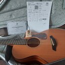 Akustická kytara v barvě přírodního dřeva umístěná v otevřeném kufru. Vedle nástroje leží dokument s nápisem „Certificate of Authenticity“ a logem „F…