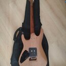 Elektrická kytara s přírodním dřevěným povrchem těla a hmatníku, položená na černém obalu. Nástroj má černý pickguard a stříbrný hardware. Na viditel…