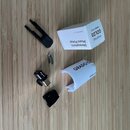 Na fotografii je phono pickup v černé barvě s kovovými prvky, doprovázený černým plastovým držákem a dvěma montážními šroubky. Vedle nich je bílá kra…