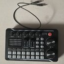 Černý ovládací panel s různými tlačítky, posuvníky a dvěma velkými otočnými knoflíky. Na zařízení jsou nápisy TREBLE, MID, BASS, RECORD, Accompany, M…