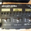 Černý multifunkční efektový procesor s nápisem ZOOM G3n Multi-Effects Processor. Zařízení má tři malé displeje, pod kterými jsou umístěny ovládací tl…
