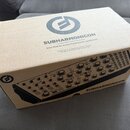 Kartonová krabice s nápisem SUBHARMONICON a textem Semi-Modular Analog Polyrhythmic Synthesizer. Na horní i boční straně je umístěno kulaté logo s pí…