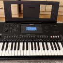Černý digitální klavír s bílými a černými klávesami. Na horním panelu je uprostřed displej s nápisem YAMAHA a vpravo označení modelu PSR-E463. Nástro…
