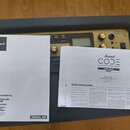 Fotografie zachycuje kousek kytarového komba s nápisem CODE 50 a logem Marshall. Před zesilovačem leží tři papírové dokumenty, z nichž jeden je uživa…