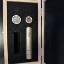Stříbrný kondenzátorový mikrofon v dřevěném kufru s černou pěnovou výplní. Na těle mikrofonu je nápis „Oktawa“ a modelové označení „MK-012-01“. Ve sp…