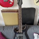 Elektrická kytara s černým matným povrchem a viditnou strukturou dřeva. Na hlavě hmatníku je bílý nápis „Solar Guitars“. Nástroj má šest strun, dva h…