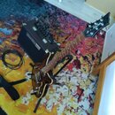 Na fotografii je hnědá polodupatá elektrická kytara s tmavým hmatníkem, umístěná na černém stojanu. Na hlavě kytary je viditelné bílé logo Epiphone.…
