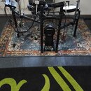 Elektronická bicí souprava s černým rámem a černými pady. Na centrálním stojanu je viditelné bílé logo Roland a pod ním nečitelný nápis. Souprava je…