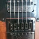 Detail elektrické kytary s černým snímačem a černým mostem na dřevěném těle. Na snímači je nápis seymour Duncan a na mostě nápis EVERTUNE®. Povrch sn…