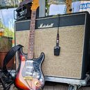 Elektrická kytara s trupem v barevnosti sunburst a hnědým hmatníkem. Na hlavě je vidět nápis Squier a na krycí desce trupu jsou různé podpisy. Kytara…