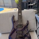 Tmavě fialová elektrická kytara s lesklým povrchem a černým hardwarem. Na hmatníku je v horní části viditelné logo „Ibanez“. Nástroj má dva humbucker…