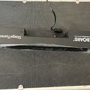 Černý kovový držák na pedály s nápisy StageTuner ST-02 a ROCKBOARD by WARWICK. Předmět je připevněn šrouby k černé texturované ploše. V horní části j…