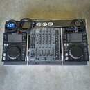 Sada DJ equipmentu v transportním kufru. Uprostřed je černý mixážní pult s nápisy ALLEN&HEATH a xone, po stranách jsou dva identické černé přehrávače…