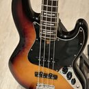 Elektrická basová kytara s korpusem v barevném přechodu od černé přes červenou k žluté. Nástroj má černý pickguard, hmatník z tmavého dřeva a chromov…