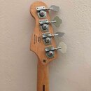 Záběr na hlavu basové kytary z přírodního dřeva se čtyřmi stříbrnými ladičkami. Na zadní straně hlavy je černý nápis „Designed & Built by Fender Cust…