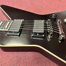 Černá elektrická kytara s výrazným, hranatým tvaru těla a bílým lemováním. Nástroj má dva černá humbuckery, jeden ovládací knoflík a přepínač. Na obo…