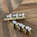 Dvě sady ladicích kolíků v pozlacené barvě s bílými plastovými knoflíky. Každá sada obsahuje čtyři ladicí mechanismy na společné kovové liště. Povrch…