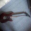 Elektrická kytara s tmavě červeným lakovaným trupem z dřeva s viditnou strukturou zrn. Nástroj má dva humbuckery, jeden tónový potenciometr a přepína…