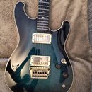 Elektrická kytara s tmavě modrým přechodovým lakem a krémovým lemováním korpusu. Nástroj má dva humbuckery s kovovými kryty, jeden ovládací přepínač…