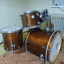 Sada bubnů v hnědé dřevěné povrchové úpravě. Na jednom z tom-tomů je viditelný kulatý štítek s nápisem "GRAND VINCENT". Soubor obsahuje basový buben,…