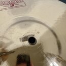 Detailní pohled na mosazný činel s centrálním otvorem. V horní části je viditelné logo Paiste 2002 a nápisy TRADE MARK oraz MADE IN SWITZERLAND. Povr…