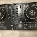 Černý DJ kontrolér se dvěma jog-wheels a centrálním mixážním sekcí. Na zařízení jsou viditelné nápisy „PERFORMANCE CONTROLLER DDJ-400“, „rekordbox“ a…