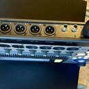 Černý digitální mixážní pult s nápisem QSC TouchMix-8. Zadní panel obsahuje šest XLR konektorů, dva jack konektory s popisky Aux 3/4 a Phones, USB po…