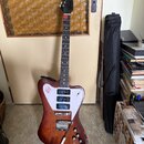 Elektrická kytara s hnědým trupem z dřeva a bílým pickguardem. Na pickguardu je červenobílý nápis "Rickenbacker". Trup vykazuje viditelné opotřebení…