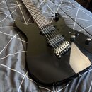 Černá elektrická kytara s lesklým povrchem a dvěma humbuckery. Nástroj má stříbrný most s pružinami a dva ovládací knofíky. Na těle nejsou vidět žádn…