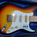 Elektrická kytara s trupem v barevném přechodu od žluté přes oranžovou k červené a černé. Nástroj má bílý pickguard, tři jednoduché snímače a tři ovl…