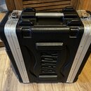Černý transportní kufr s hliníkovými hranami a dvěma kovovými zapínacími zámky. Na přední straně je vyembasovaný nápis "ROADIE". Povrch kufrů má text…