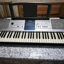Stříbrošedý digitální klavír s plastovým povrchem a černými klávesami. Na horním panelu je uprostřed logo YAMAHA a vpravo nápis PSR-E323. Nástroj je…