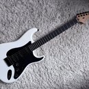 Bílá elektrická kytara s černým pickguardem a hmatníkem z tmavého dřeva. Na hlavě je viditelné logo „Fender“ a nápis „STRATOCASTER“. Nástroj má jeden…