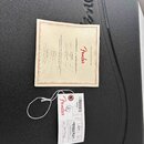 Na černém kufru s vyraženým nápisem Fender leží papírový Certifikát pravosti (CERTIFICATE OF AUTHENTICITY) značky Fender. Dokument obsahuje text „GEN…