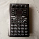 Černý sampler Roland SP-404MKII s digitálním displejem uprostřed. Horní část obsahuje čtyři otočné ovladače a řadu tlačítek pro efekty, jako jsou FIL…