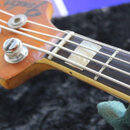 Detail hlavy a horní části hmatníku basové kytary z dřeva s lakovaným povrchem. Na hlavě je viditelné částečné logo Fender a čtyři kovové ladičky. Hm…