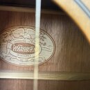 Detail vnitřní strany akustické kytary s oválnou štítkem z papíru. Na štítku je nápis CELEBRATING 125 YEARS, logo WASHBURN, text OF EXCELLENCE a ORIG…