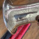 Detail stříbrného nebo niklovaného zvonu dechového nástroje s bohatým rytím květinových a listových ornamentů. Na povrchu je vyryt nápis V. KOHLERT,…